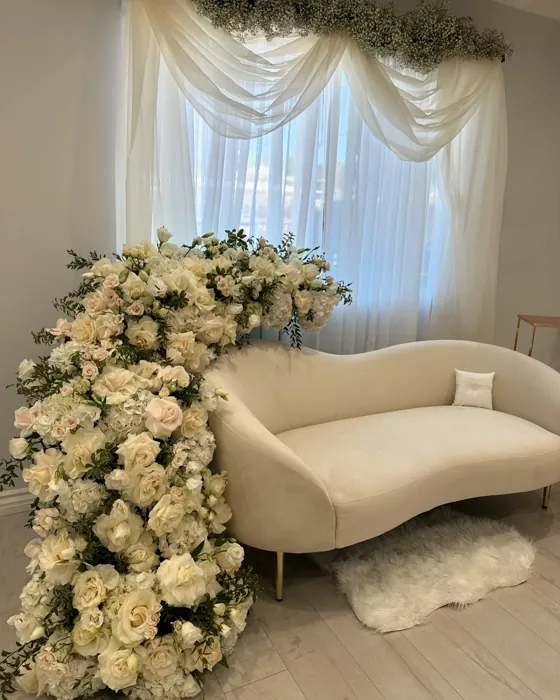 Cascading white rose and ranunculus installation beside a cream lounge sofa