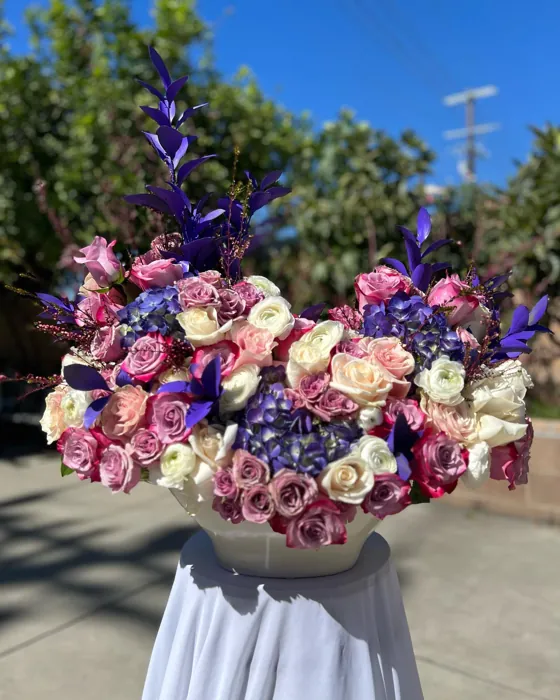 Purple hydrangea, rose and delphinium arrangement on a draped stand