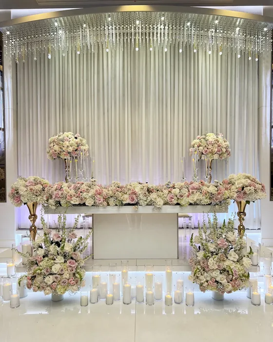 Wedding sweetheart table with blush floral garland, candles and draped crystal backdrop